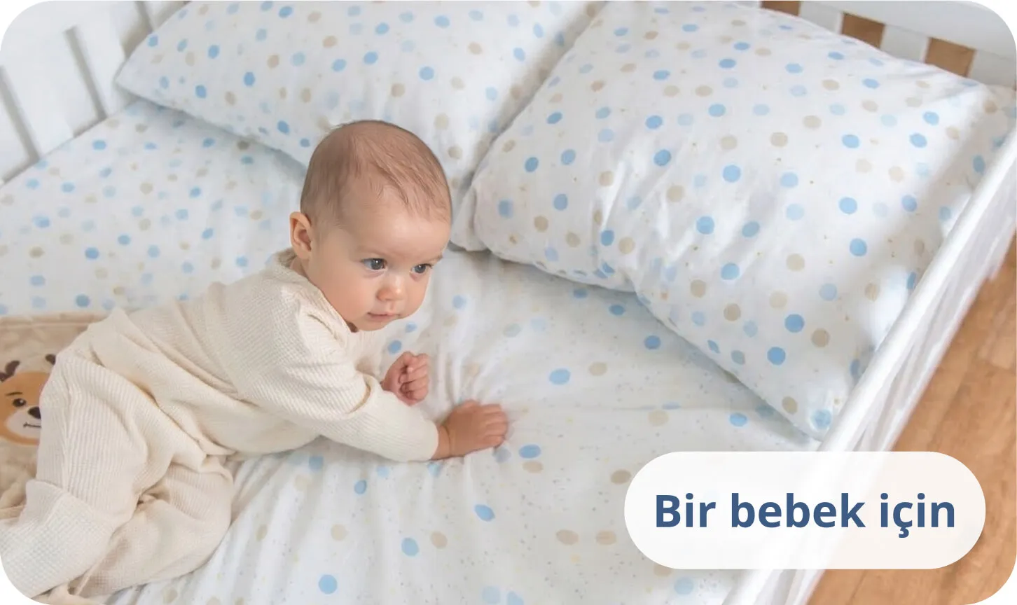Mavi puantiyeli nevresimler içinde beyaz bir yatakta karnının üzerinde yatan bebek.
